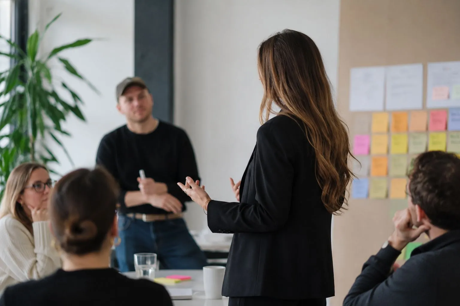 Workshop-Situation: Christine Maier steht vor einer Gruppe, im Hintergrund eine Pinnwand mit Haftnotizen